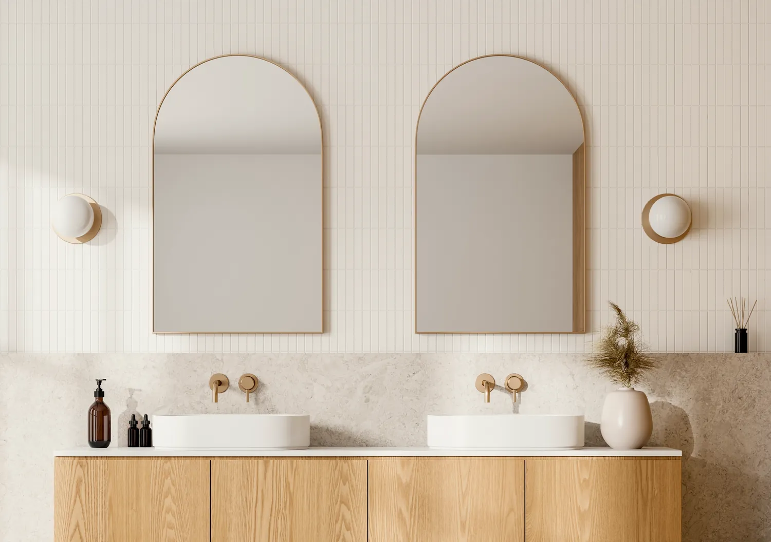 Twin arched brass-framed mirrors over stone and oak vanity joinery with wall-mounted brass tapware.